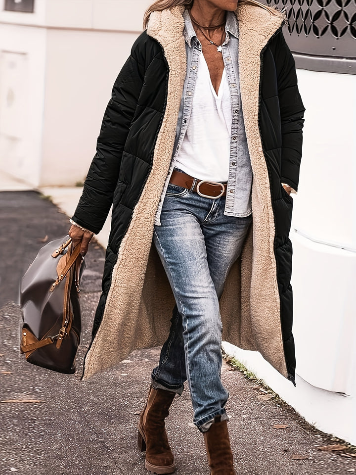 Front view, model in a black reversible quilted hooded coat with cream sherpa lining, jeans, and brown boots