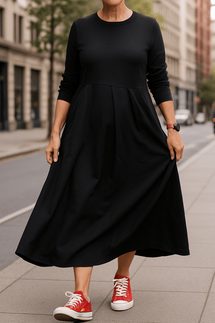 Front view, model wearing a black oversized long sleeve dress with a round neck, pockets and a pleated skirt