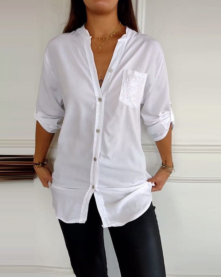Front view of a model wearing a white button blouse with sequined placket and pocket, hands on hem