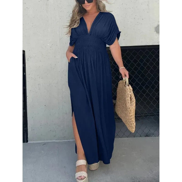 Front view of model wearing a navy elegant summer maxi dress with pockets, side split and a woven bag