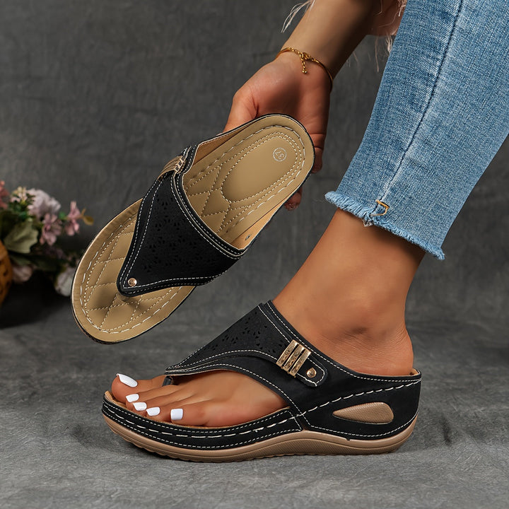 Close up of black leather sandals with white stitching, one worn by model, one held showing comfort sole