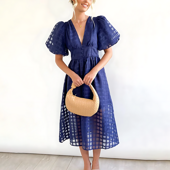 Front view of a model wearing an elegant blue summer midi dress with a textured woven handbag