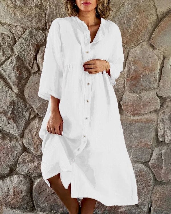 Front view of a model wearing a white loose shirt midi dress with white buttons against a stone wall