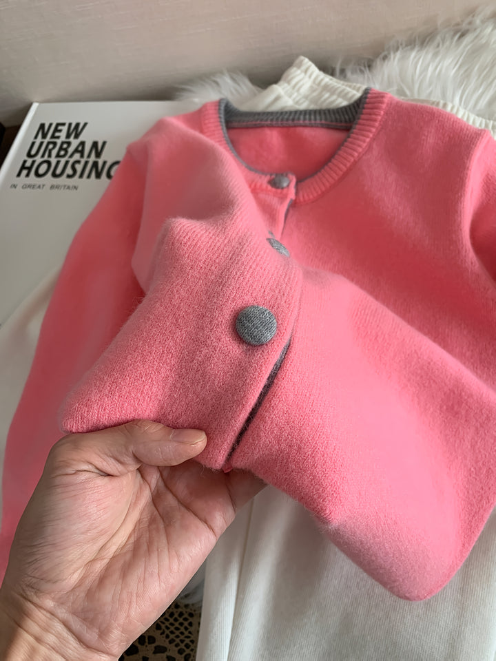 Close up of a hand holding a pink knitted buttoned cardigan with grey trim and buttons