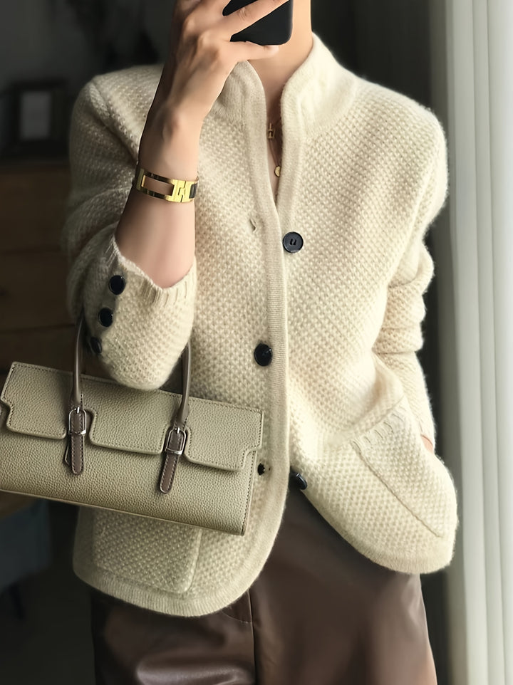 Front view of a model wearing a cream buttoned high-neck cardigan with a gold bracelet and a light green handbag