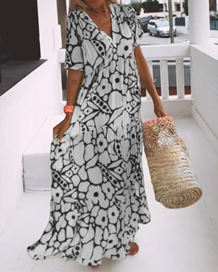 V neck printed maxi dress, side view worn by model, holding a straw bag and walking on a balcony