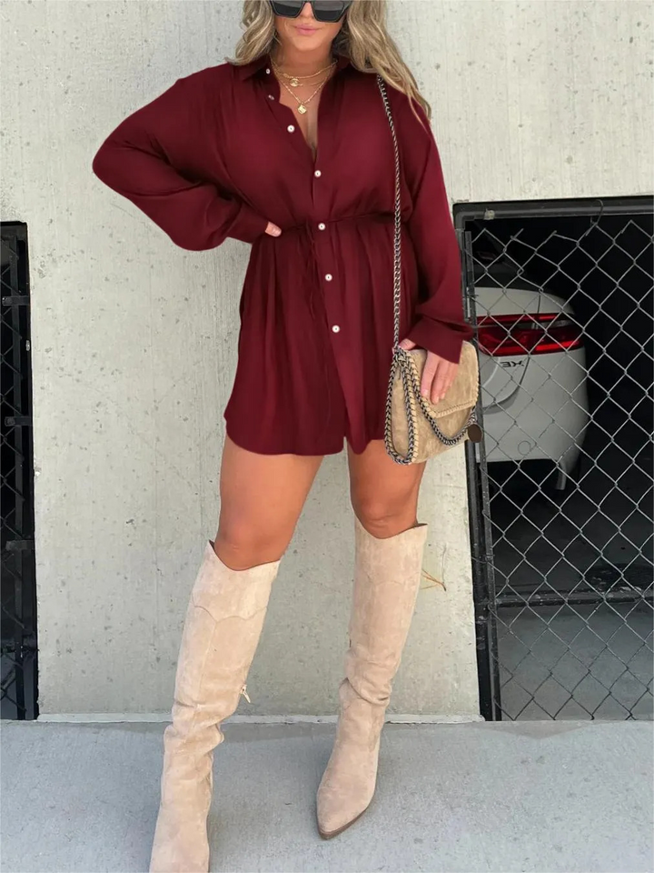 Front view, model wearing a burgundy satin romper with a self-tie belt and beige knee high boots, alternate angle