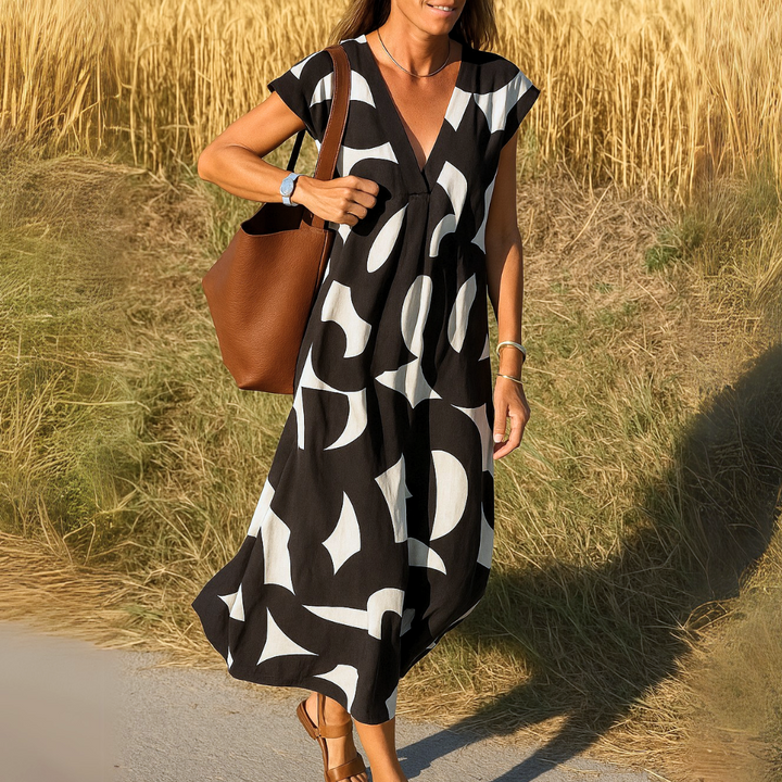 Three quarter view of a woman wearing a black and white patterned flowing V-neck boho dress with a brown bag
