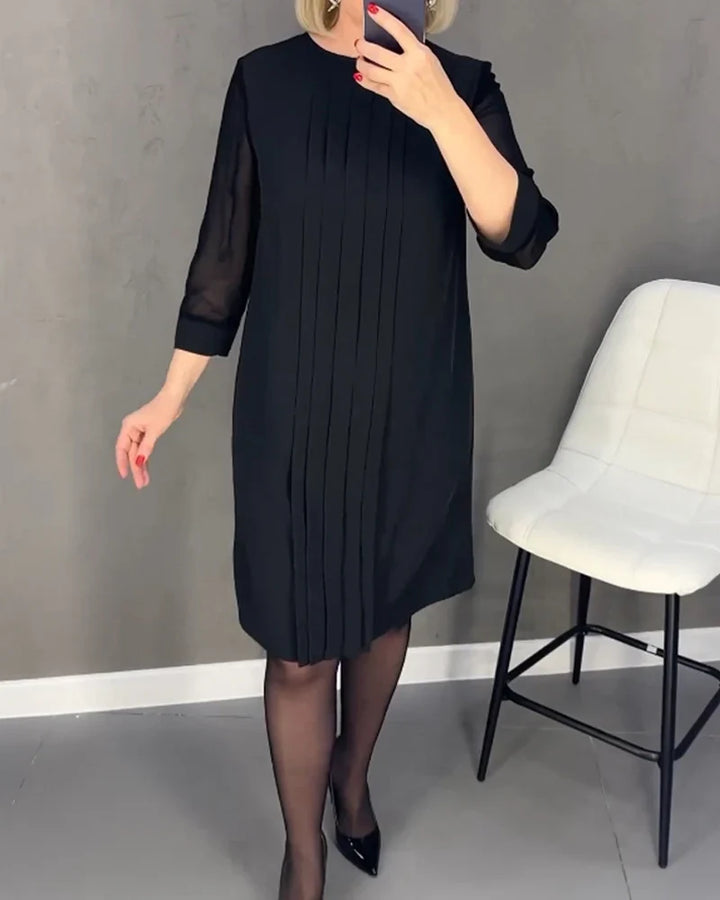 Front view, model wearing a black pleated knit dress with sheer three quarter sleeves and black heels