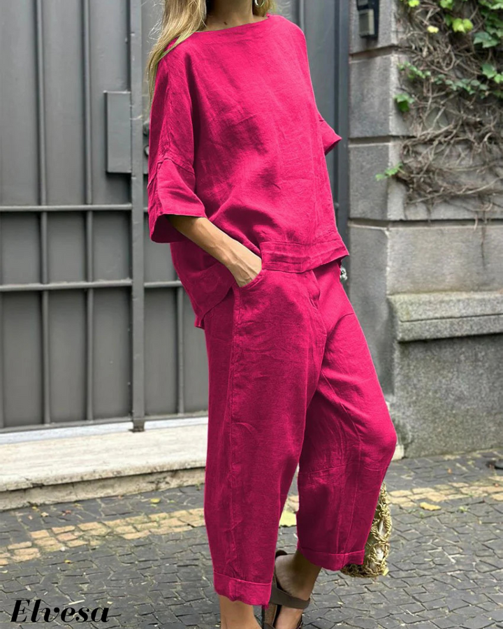 Three quarter view, model wearing a bright pink two piece set with a boat neck top and cuffed pants, hand in pocket