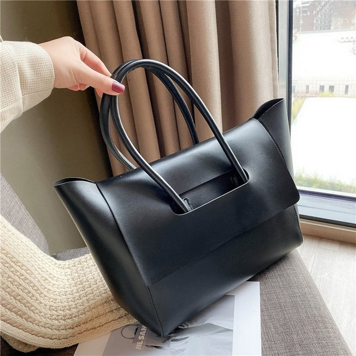 Close up of a hand holding the top handle of a black Geneva vegan leather handbag by a window