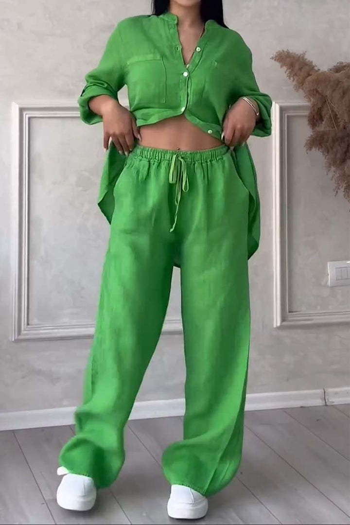 Front view of a model in a bright green long sleeve blouse and wide leg pants set with hands on waistband