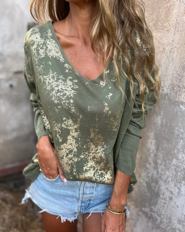 Close up of a model wearing the relaxed knit top with gold details and a V-neckline, paired with denim shorts