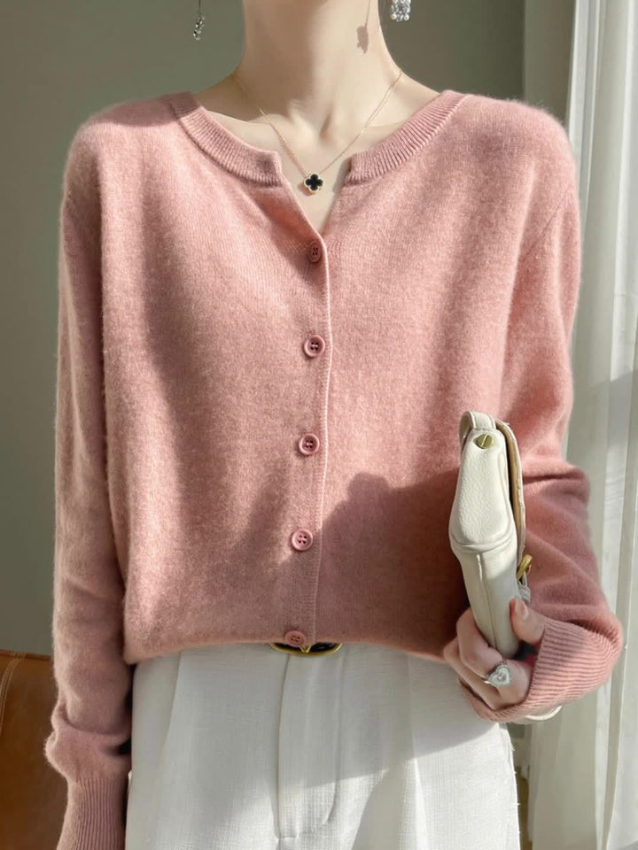 Front view of a model wearing the pink buttoned knit cardigan with a black clover necklace and white pants
