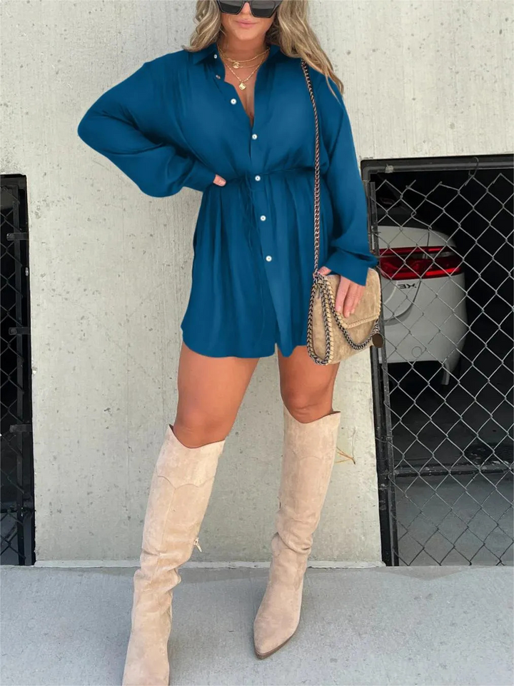 Front view, model wearing a teal satin romper with a self-tie belt and beige knee high boots