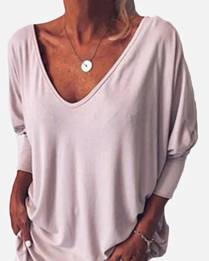 Front view of a model wearing a light grey linen V-neck blouse with 3/4 sleeves and a round pendant