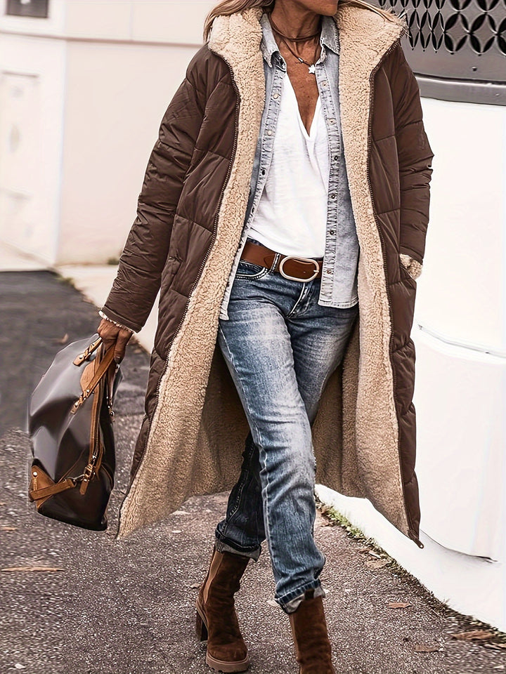 Three quarter view, model wearing a brown reversible quilted hooded coat with cream sherpa lining over a white top and jeans