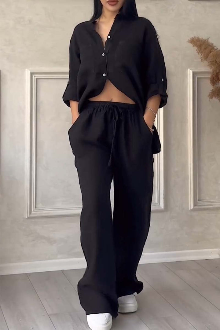 Front view of a model in a black long sleeve blouse and wide leg pants set with hands in pockets