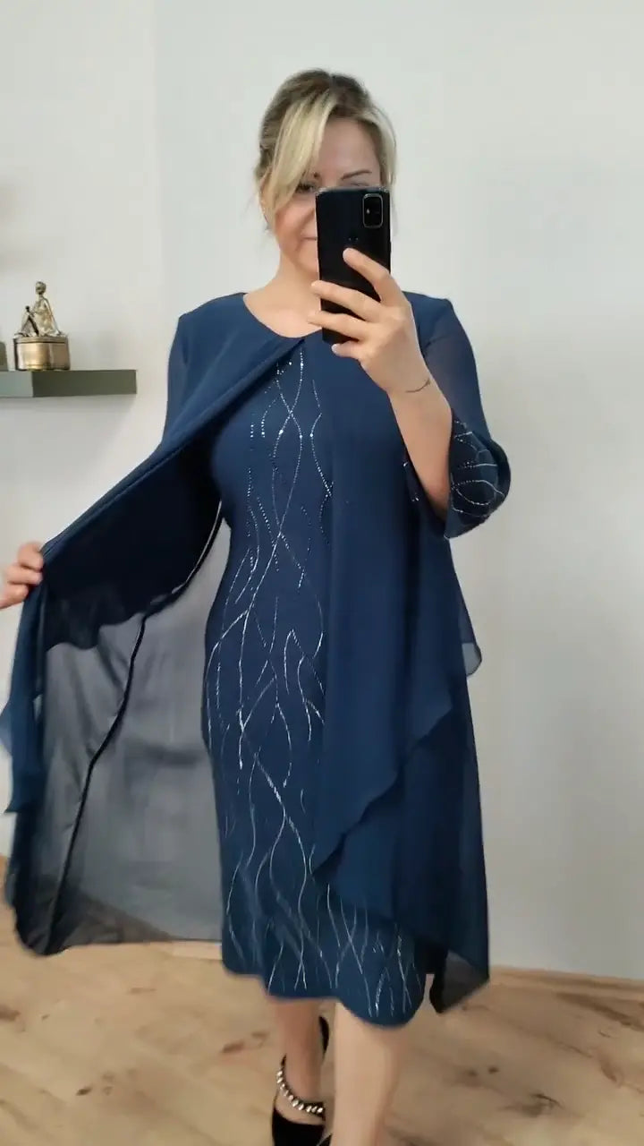 Front view of a model in a navy elegant chiffon ruffle midi dress with silver patterns taking a mirror selfie
