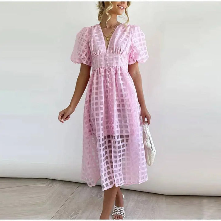 Front view of a model wearing an elegant pink summer midi dress with a square pattern and a white woven handbag