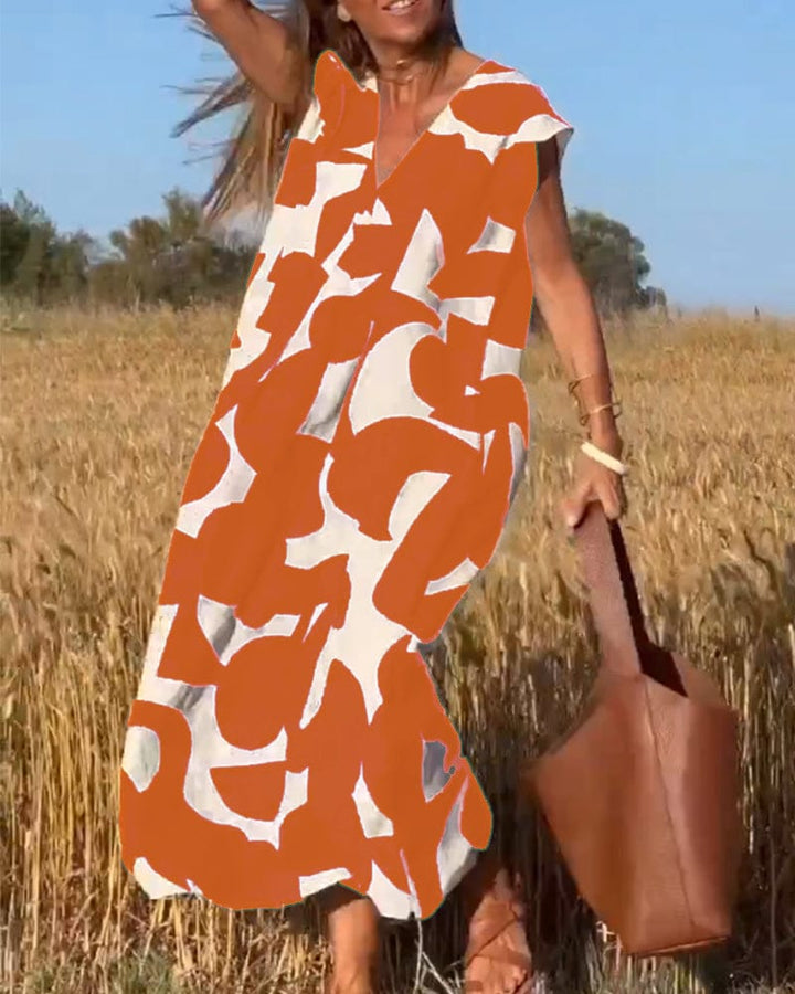 Front view of a model in an orange and white abstract print vintage long dress with a brown leather tote bag