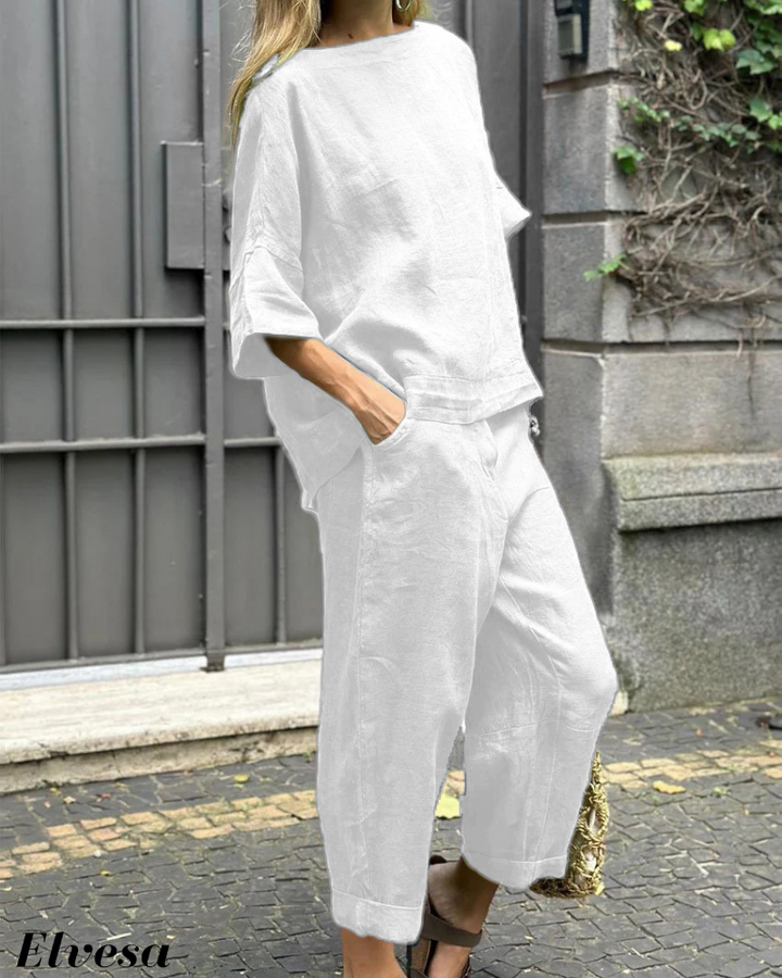 Side view, model wearing a white two piece set with a boat neck top and cuffed pants, hand in pocket