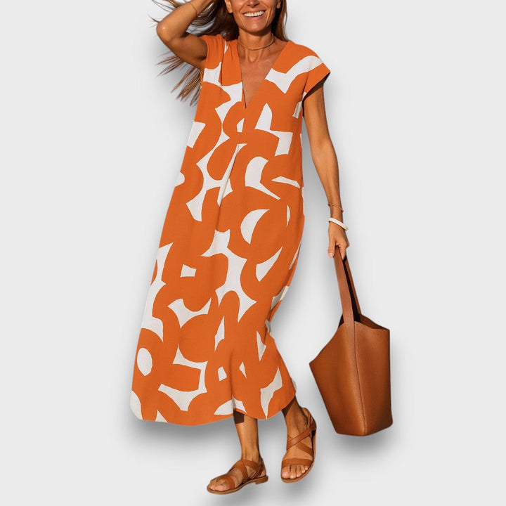 Three quarter view, model wearing airy V-neck dress with orange and white abstract pattern, brown sandals and shoulder bag