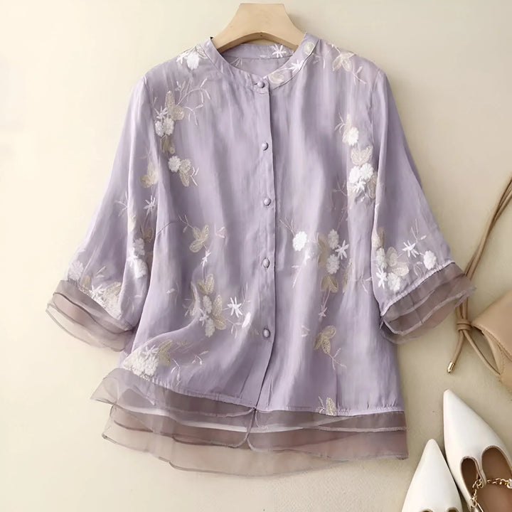 Flat lay of a purple lightweight cotton blouse with delicate floral embroidery and a sheer layered hem