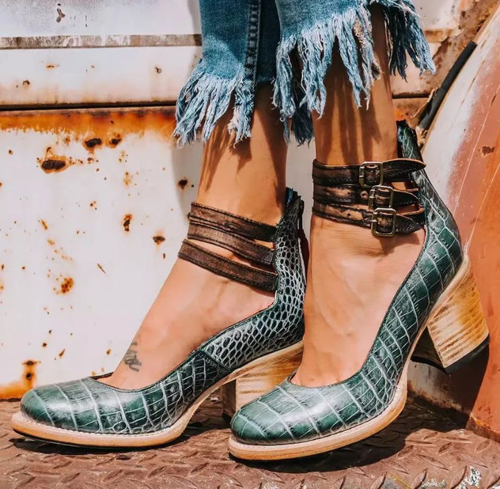 Worn by model, elegant vintage heeled sandals in a dark teal crocodile texture with triple buckled ankle straps