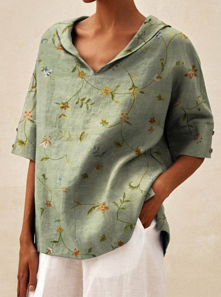 Front view of a model wearing a green V-neck floral top with rolled up sleeves, hand in pocket