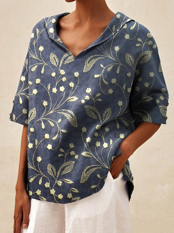 Close up front view of a model wearing a navy V-neck floral top with white flowers, hand in pocket