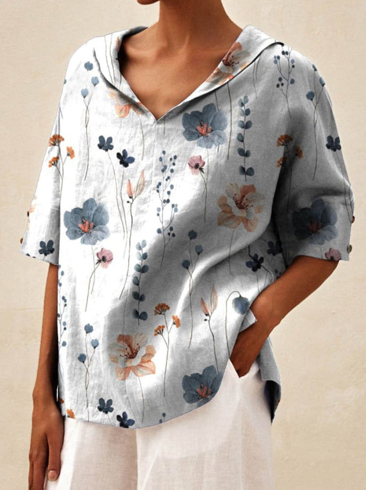 Front view of a model wearing a white V-neck floral top with blue and orange flowers, hands in pockets