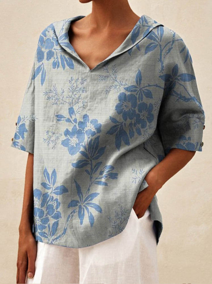 Close up front view of a model wearing a grey V-neck floral top with blue flowers, hand in pocket