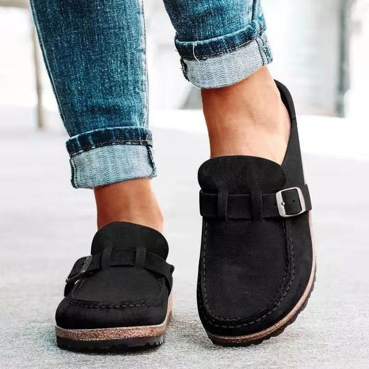 Close up worn by model of black suede loafers with buckle and stitching detail on the upper
