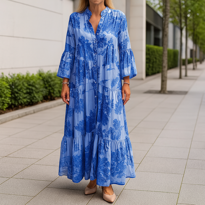Front view of an elegant floral dress worn by model, a long blue cotton blend dress with tiered skirt and bell sleeves