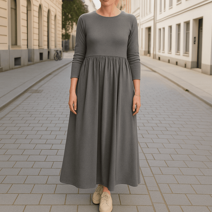 Front view of a woman wearing a grey flowy knitted midi dress with long sleeves on a paved street