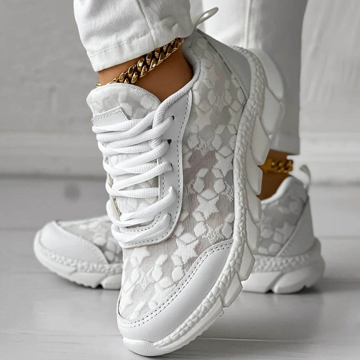 Front view, white breathable orthopedic boots with floral lace detail worn by model with gold anklet