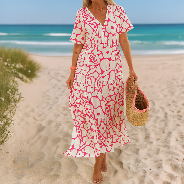 Front view, model in a white and pink patterned summer dress walking barefoot on a sandy beach