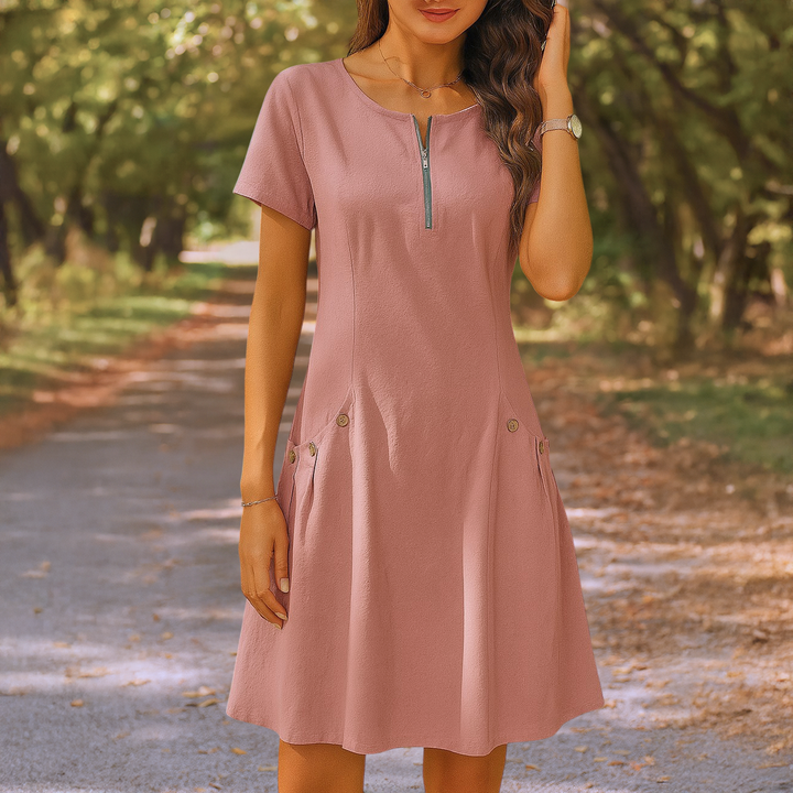 Front view of a model wearing the pink Millie summery dress with zip detail and decorative buttons on pockets