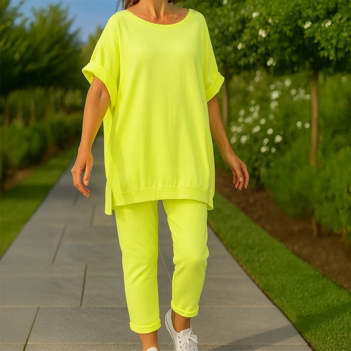 Front view of a model wearing a neon yellow loose sweatshirt and trousers set with white sneakers on a path