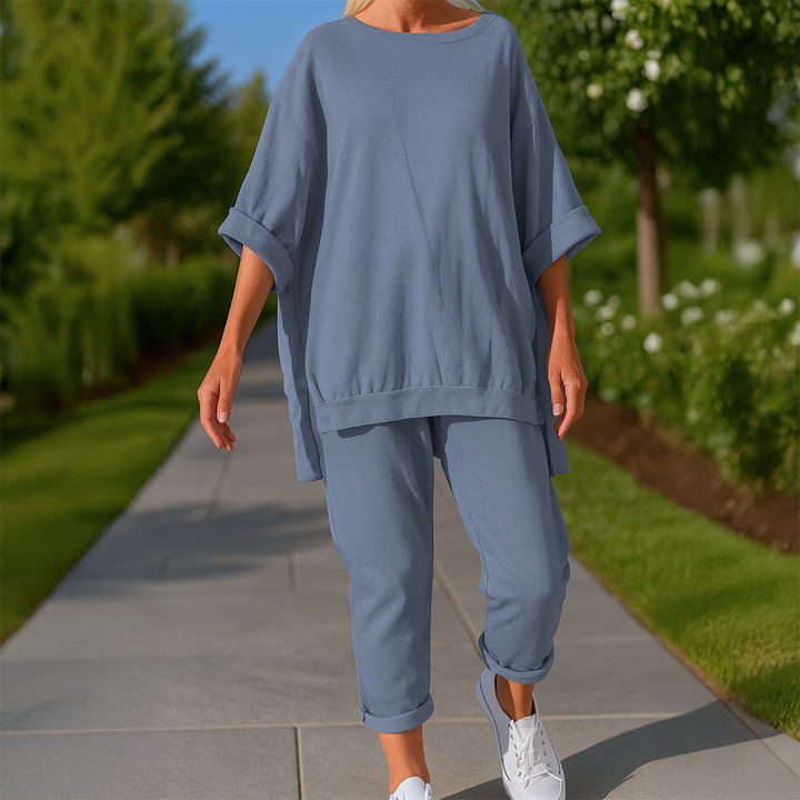 Front view of a model in a denim blue loose sweatshirt and trousers set with white sneakers on a path