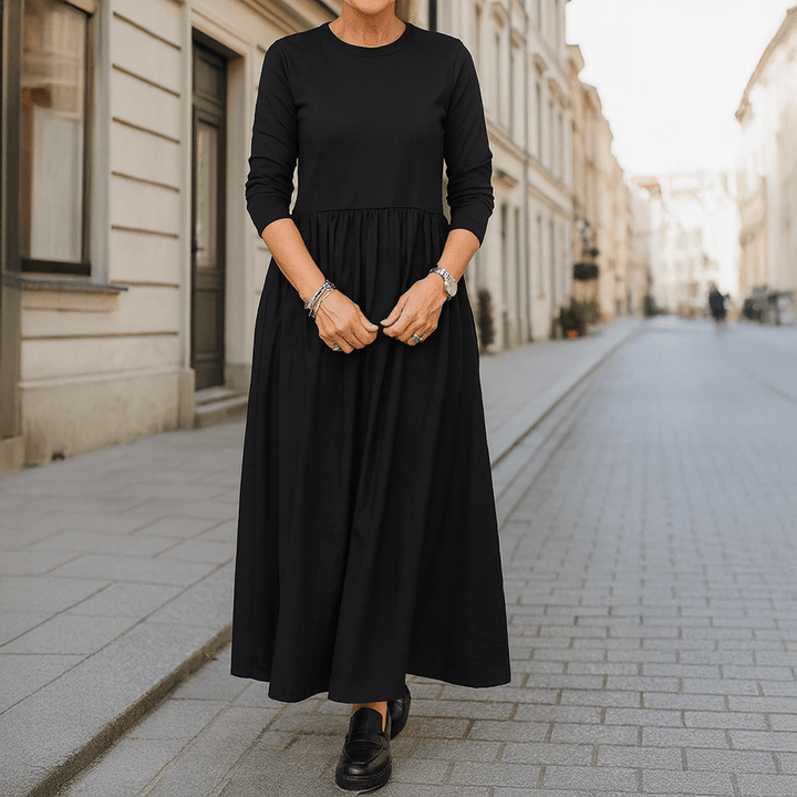 Front view of a woman wearing a black flowy knitted midi dress with long sleeves and pleated skirt detail