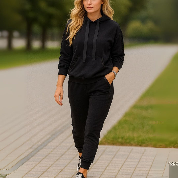 Front view of a woman walking in a black sequin patchwork hoodie tracksuit set on a paved path