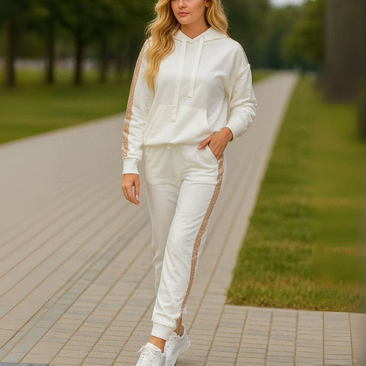 Front view of a woman in a white sequin patchwork hoodie tracksuit set with white sneakers on a path