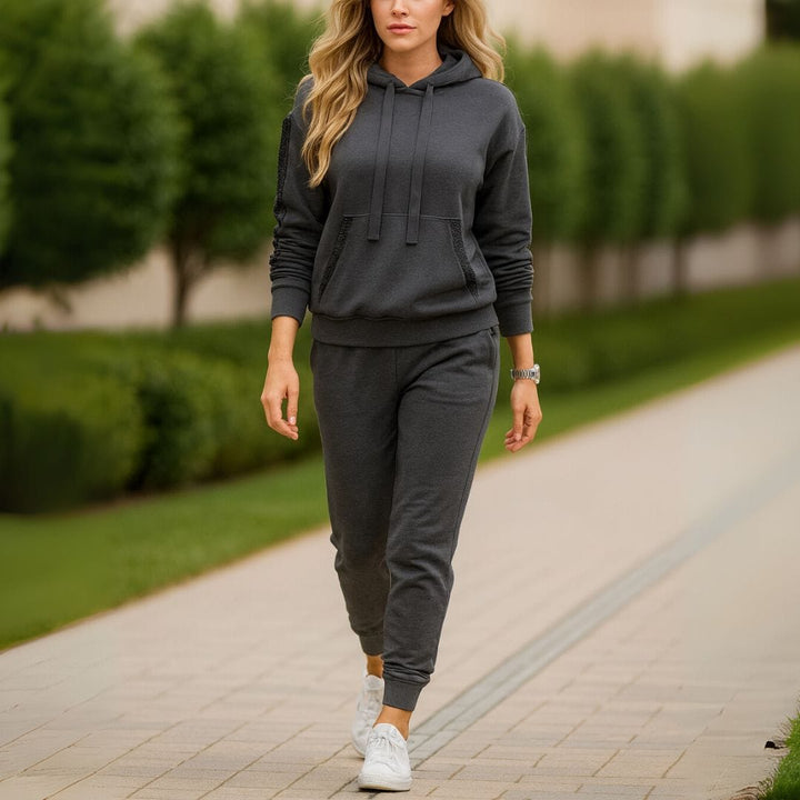 Front view of a woman walking in a charcoal sequin patchwork hoodie tracksuit set with white sneakers on a path