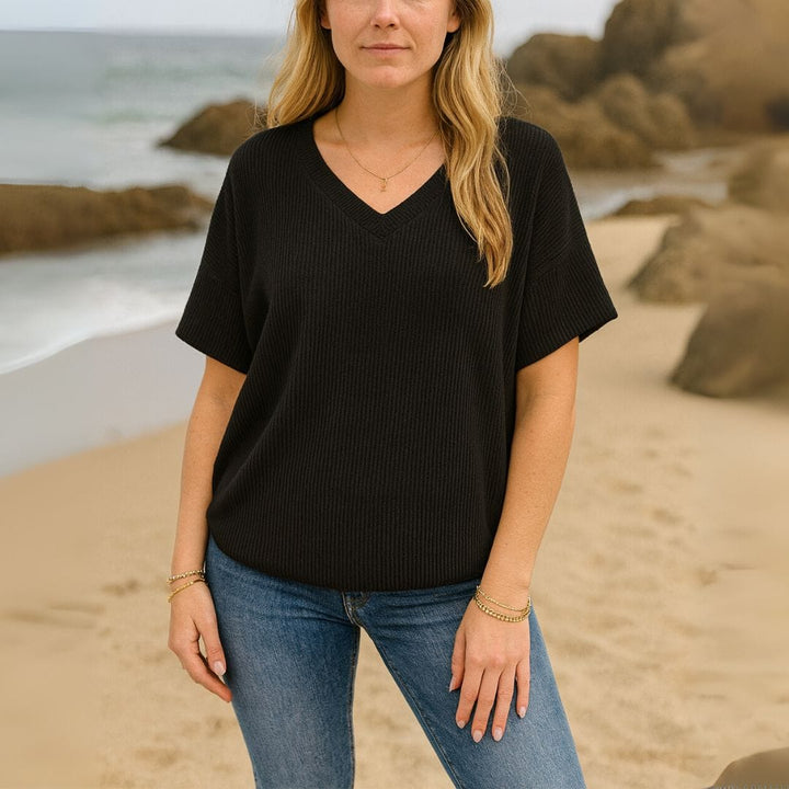 Front view of a woman wearing a black V-neck t-shirt and blue jeans on a sandy beach