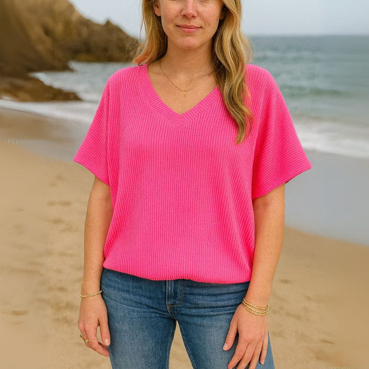 Front view of a woman wearing a bright pink V-neck t-shirt and blue jeans on a sandy beach