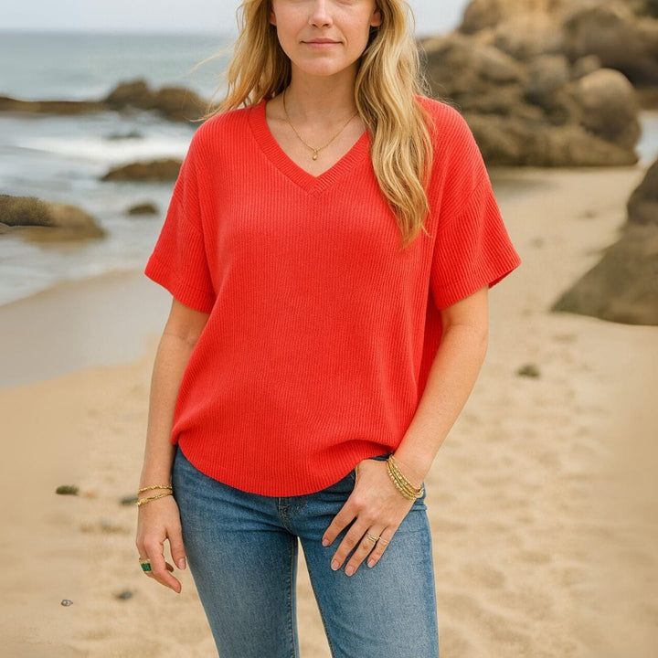 Front view of a woman wearing a red V-neck t-shirt and blue jeans on a sandy beach