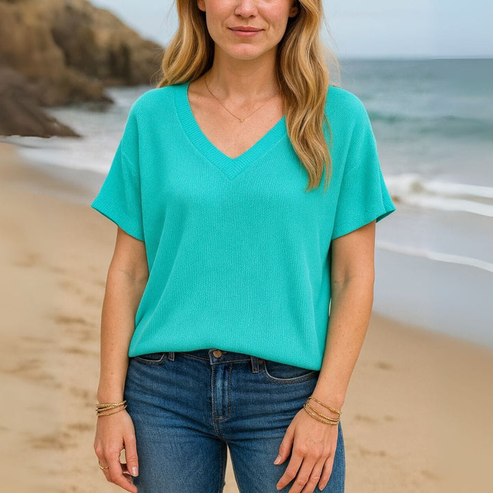 Front view of a woman wearing a teal V-neck t-shirt and blue jeans on a sandy beach