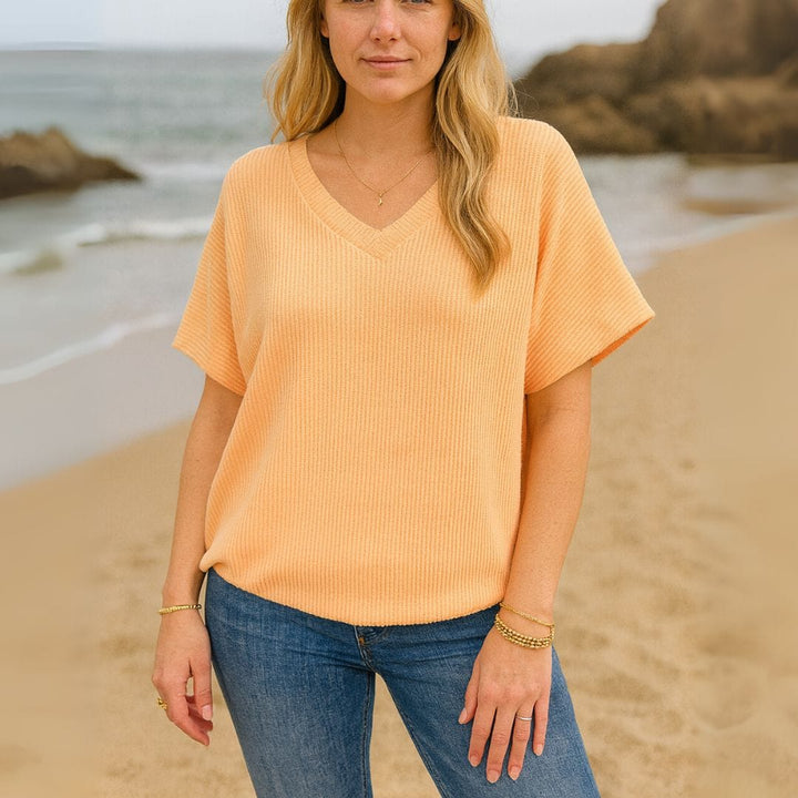 Front view of a woman wearing a light orange V-neck t-shirt and blue jeans on a sandy beach